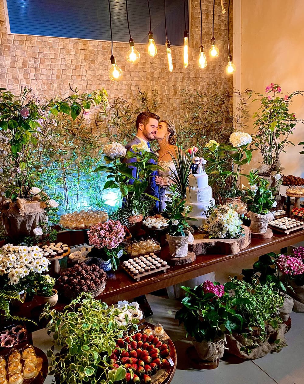 Mesa de doces e bolo decorada com plantas e luzes